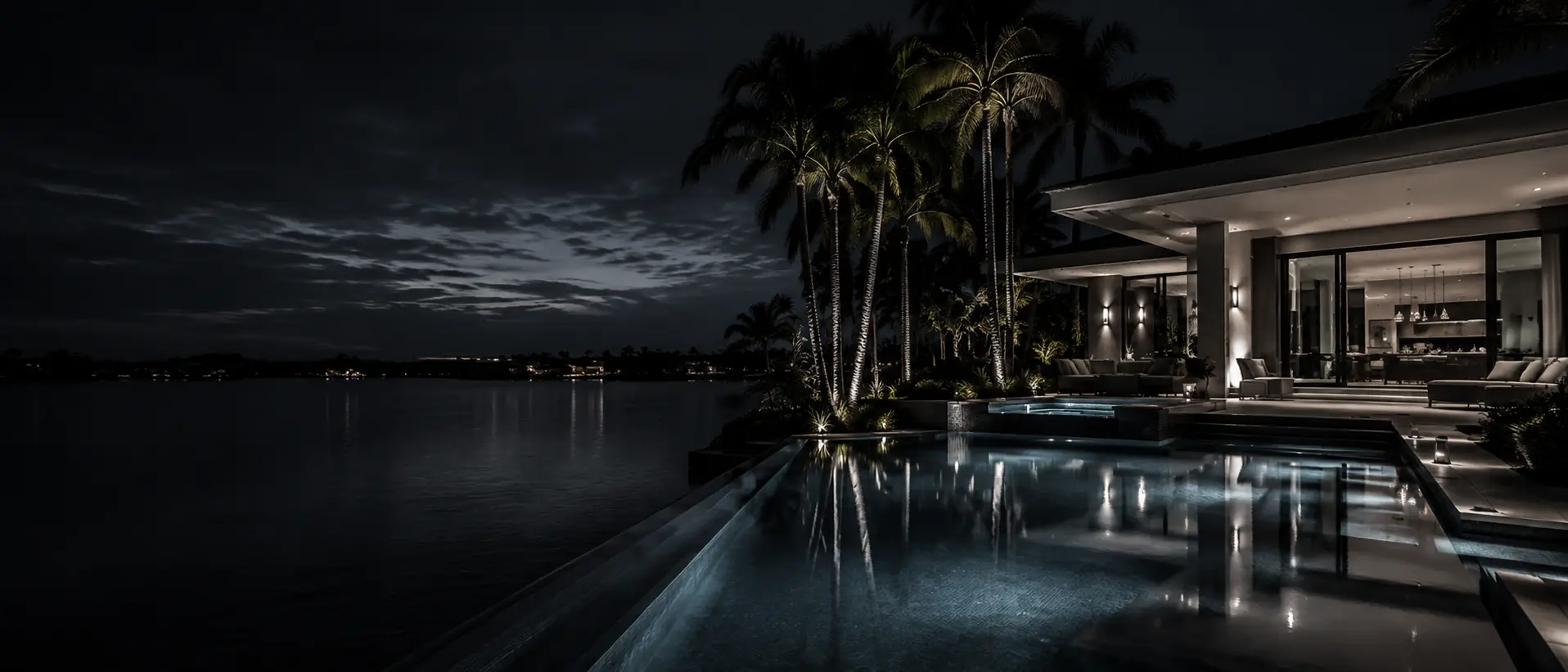 Illuminated waterfront pool and spa at night with palm trees and Intracoastal views